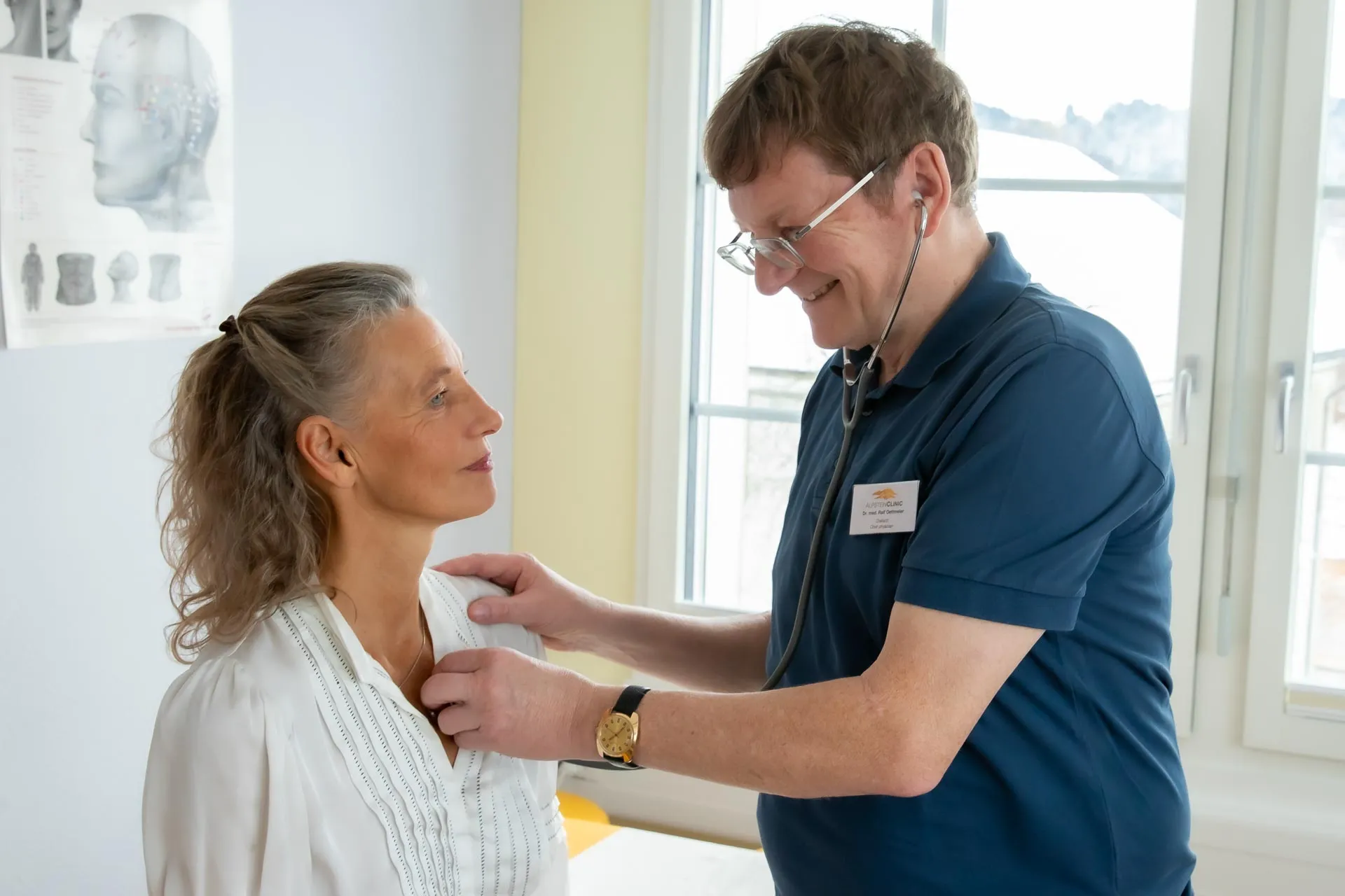 Herr Dr. med. Oettmeier hört eine Patientin mit dem Stethoskop ab