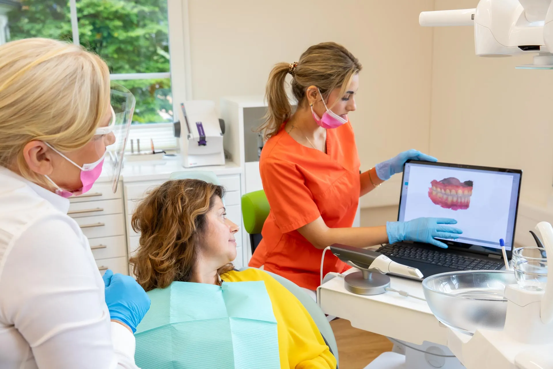 eine Dentalassistentin und eine Zahnärztin zeigen einer Patientin den Scan Ihres Kiefers