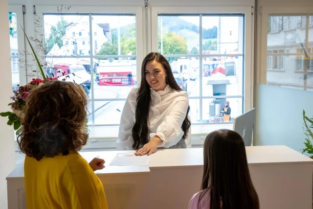 The practice administrator, Altina Kastrati, welcomes two patients and gives them a form.